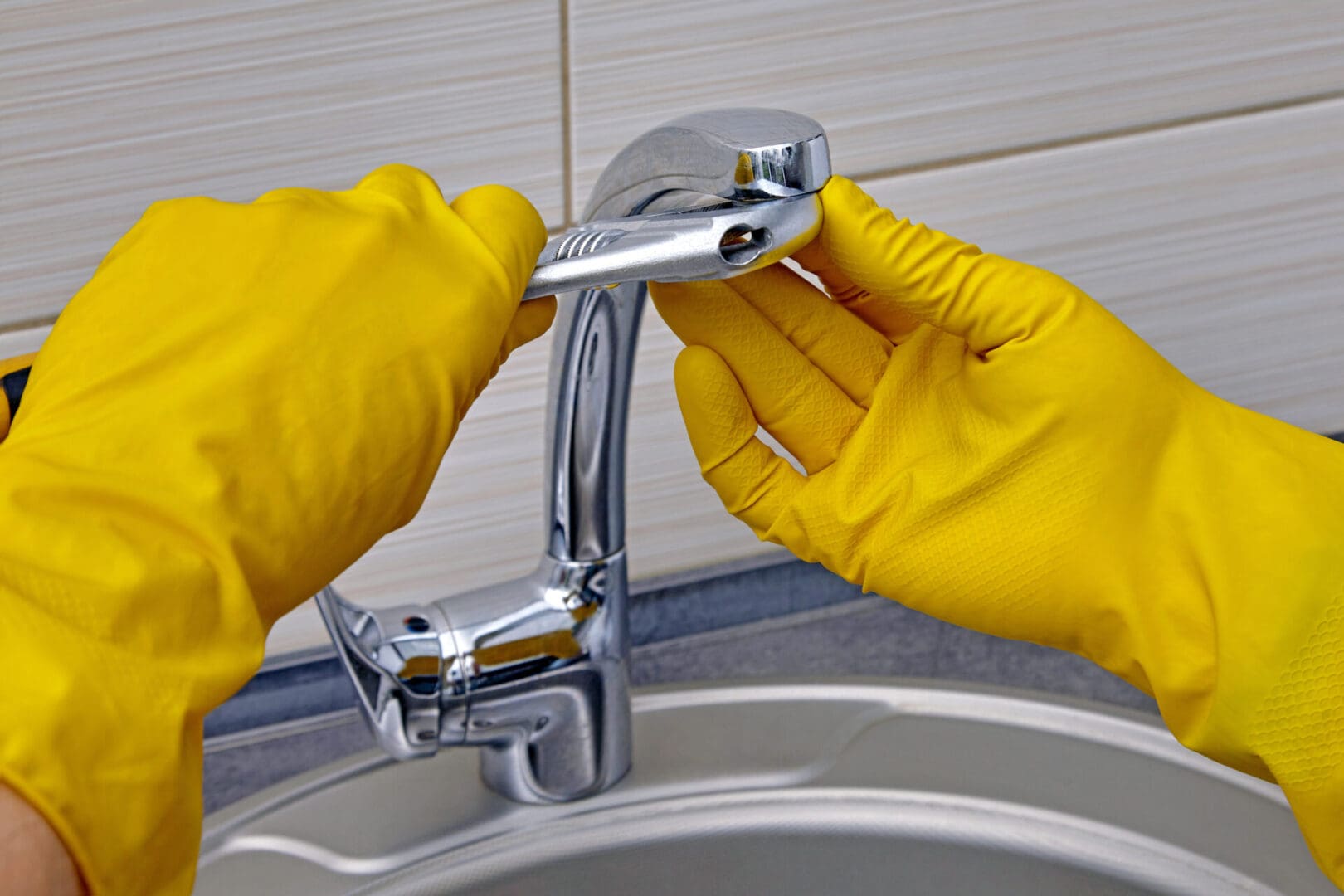 Hands in yellow gloves fixing faucet.