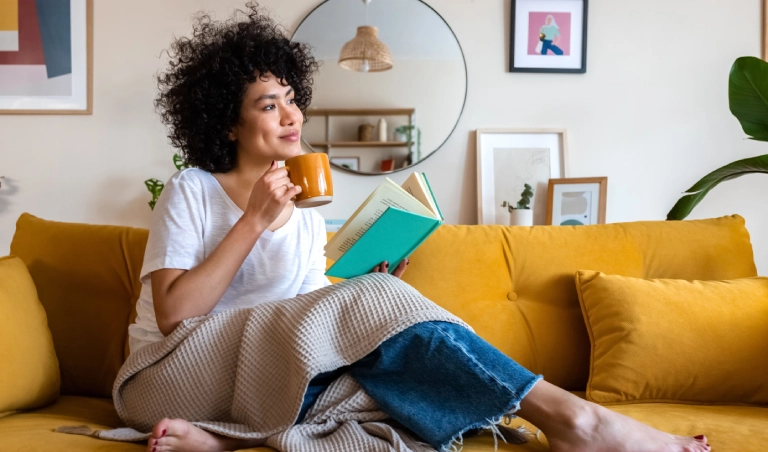 Woman reading and drinking coffee on couch.
